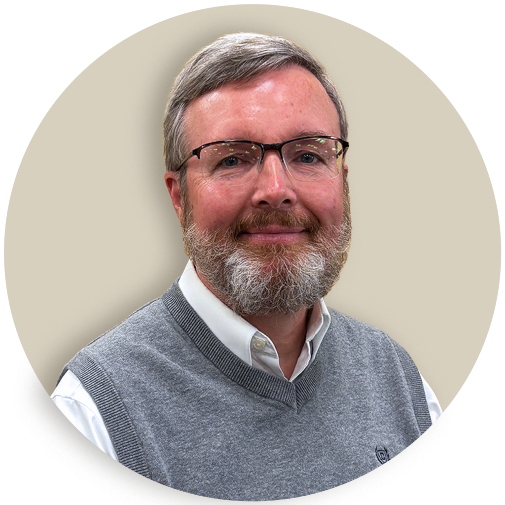 Portrait of Brian Messner with glasses and a gray beard wearing a gray sweater vest over a white shirt
