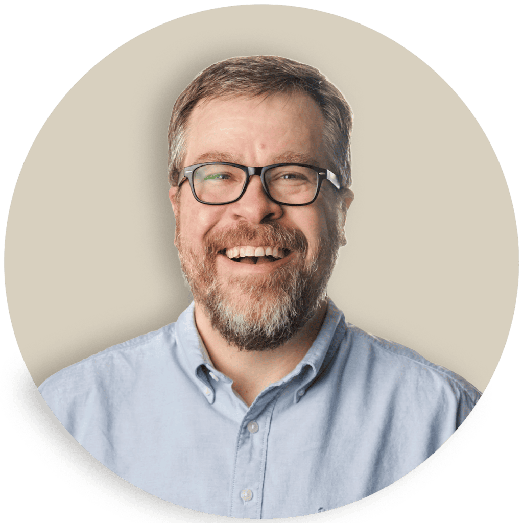 Doug Welch with glasses and a beard in a light blue shirt on a beige background